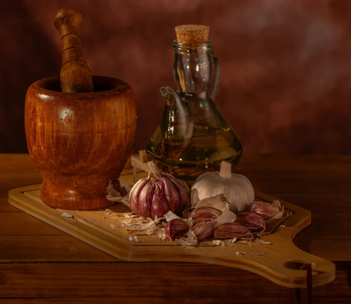 Knoblauchzehen mit Mörser und Öl auf einem Holzbrett
